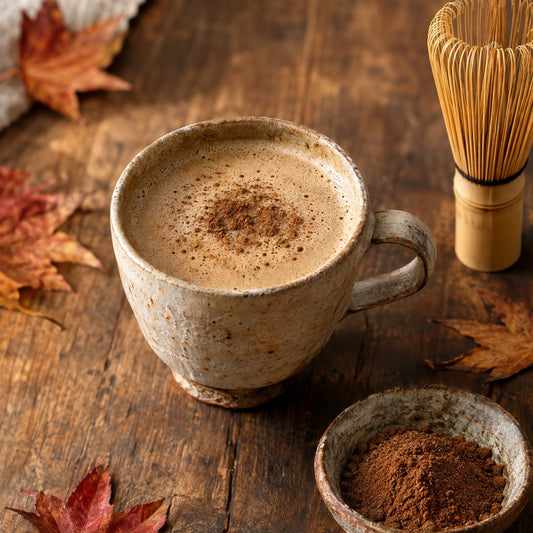 Hojicha latte in a ceramic cup with hojicha powder and bamboo whisk
