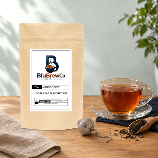 BluBrewCo Mango Treat original bag with a glass tea cup and mesh infuser, on warm wood against a sea-salt wall