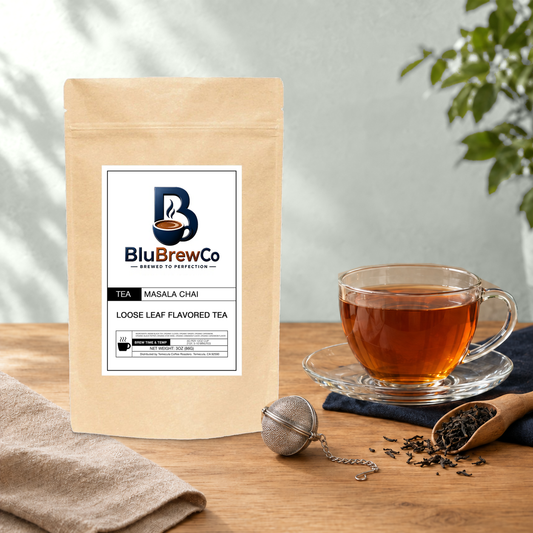 BluBrewCo Masala Chai original bag with a glass tea cup and mesh infuser, on warm wood against a sea-salt wall